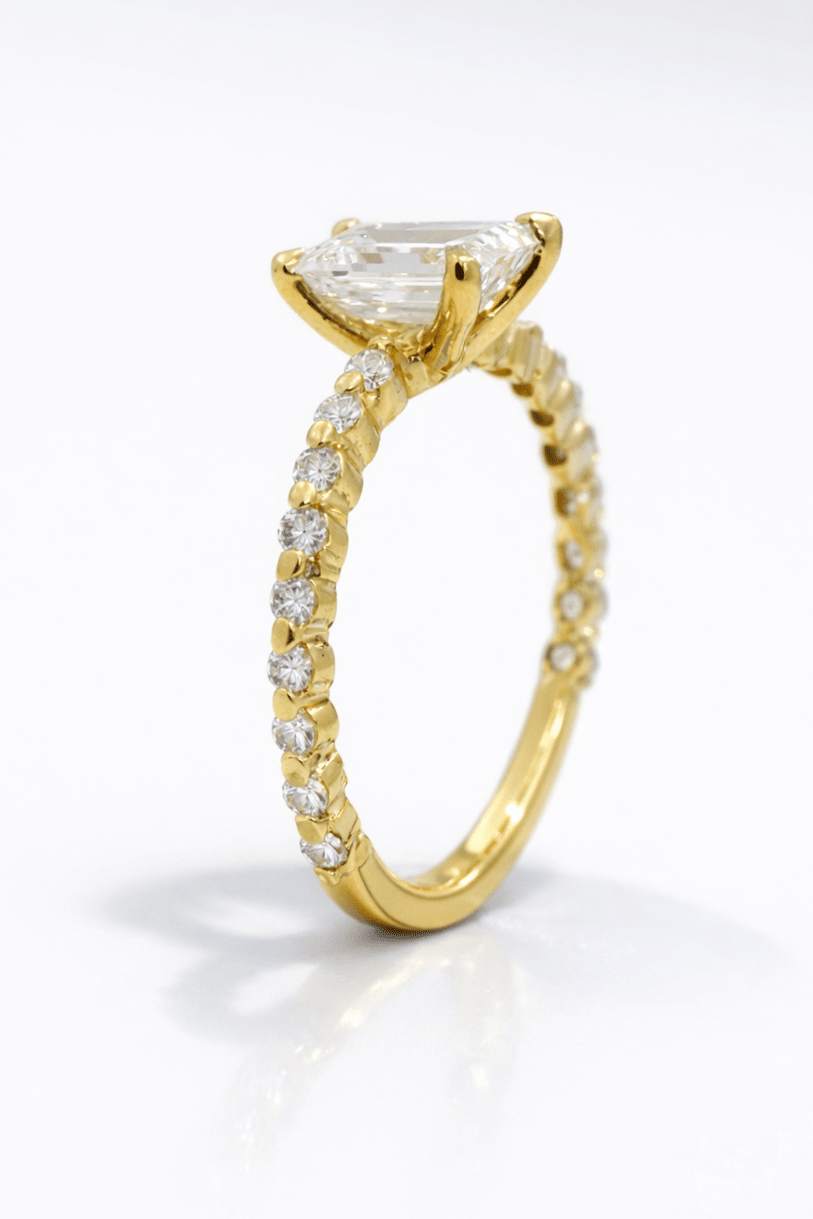 Gold ring with a large diamond and smaller diamonds on the band against a white background