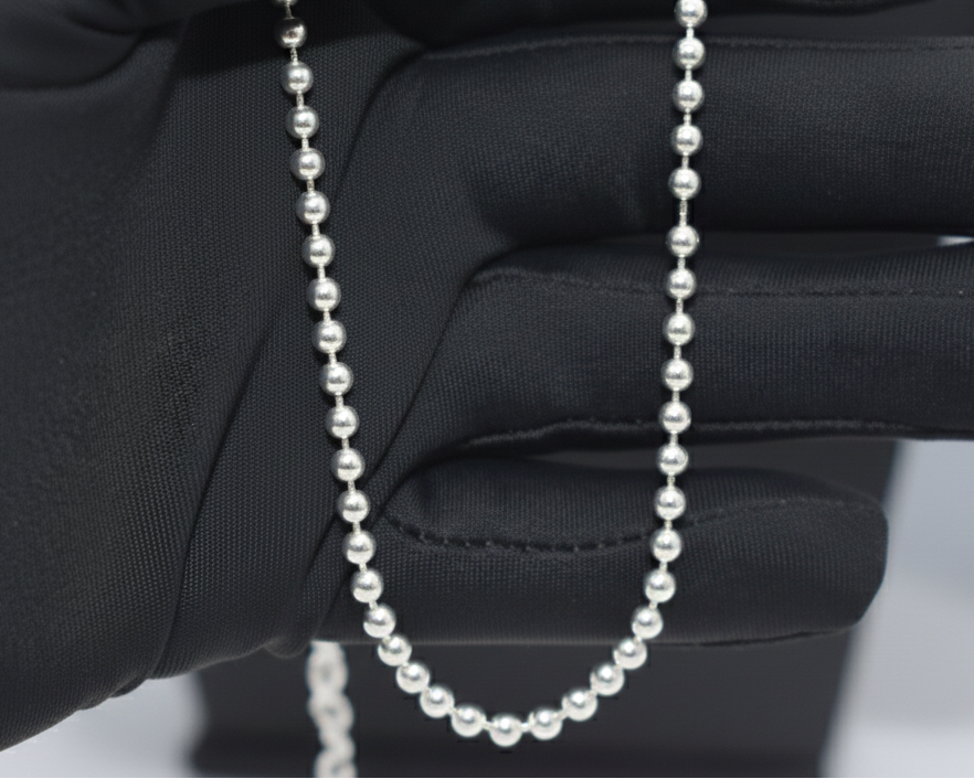 Silver beaded necklace held by a gloved hand against a white background