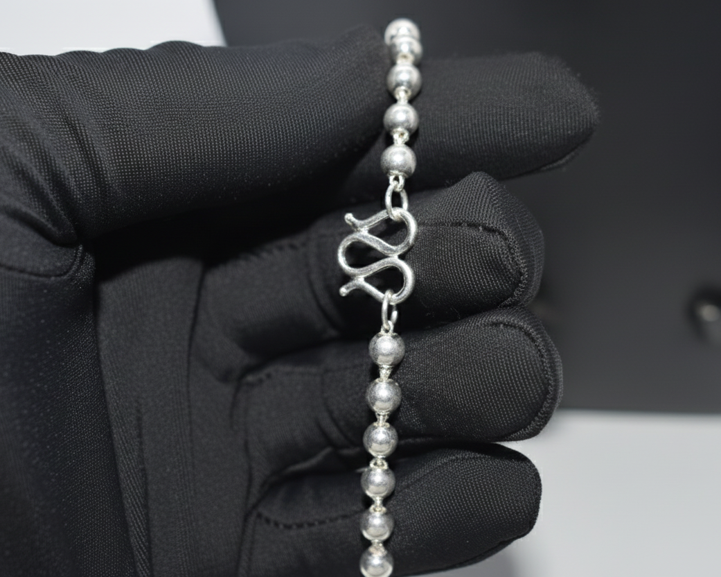 Silver bracelet with a unique design held by a gloved hand against a neutral background