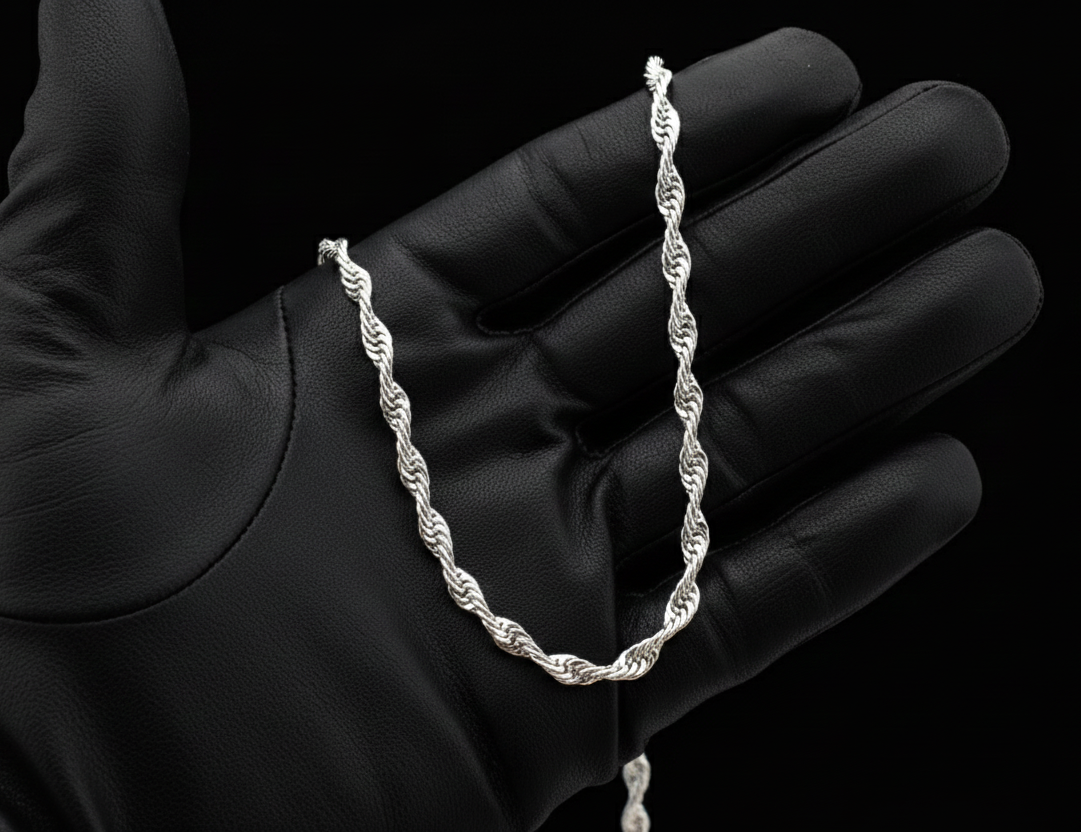 Silver rope chain held in a black gloved hand against a black background