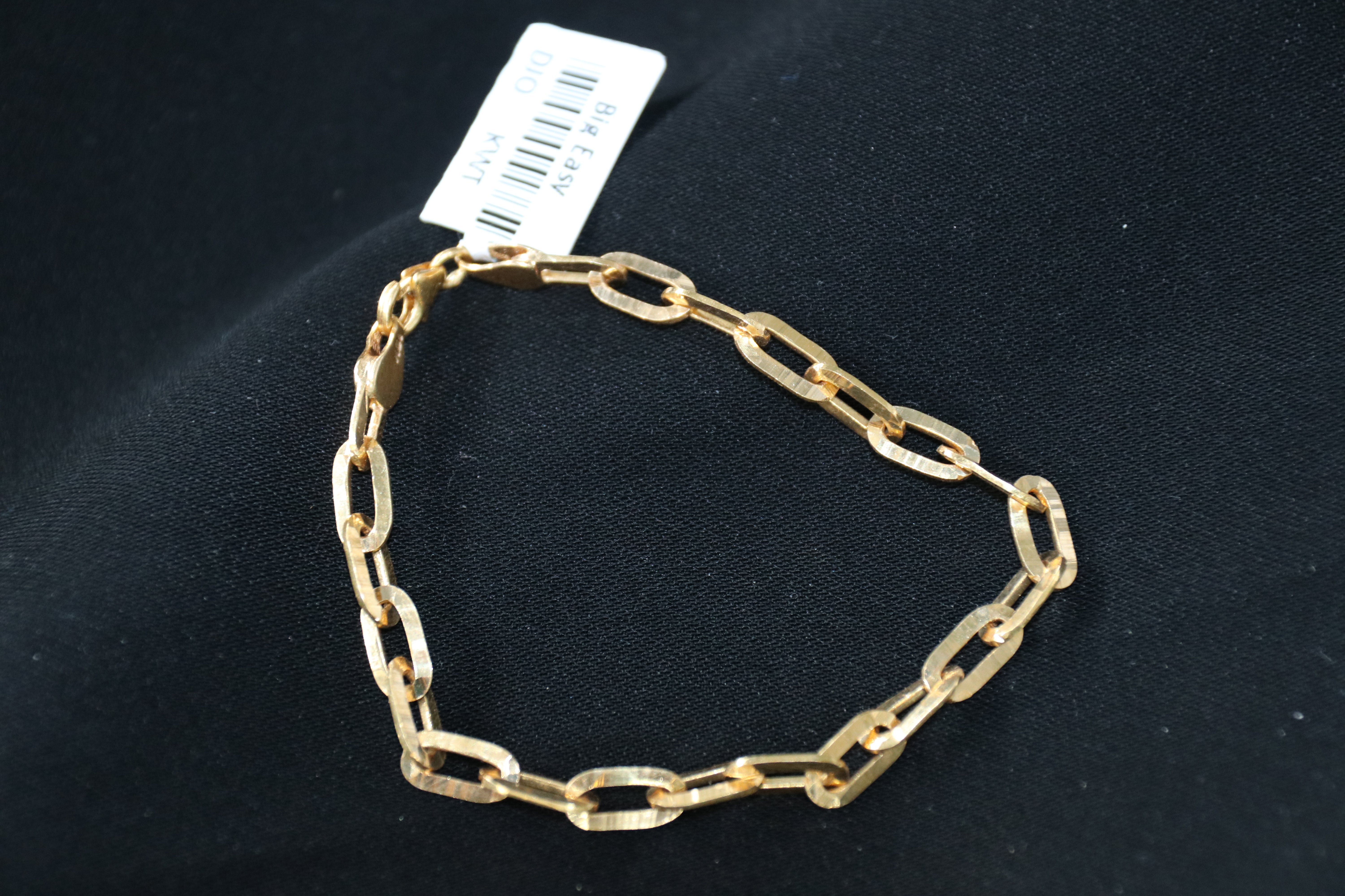 Gold chain bracelet on a black background with a tag attached.
