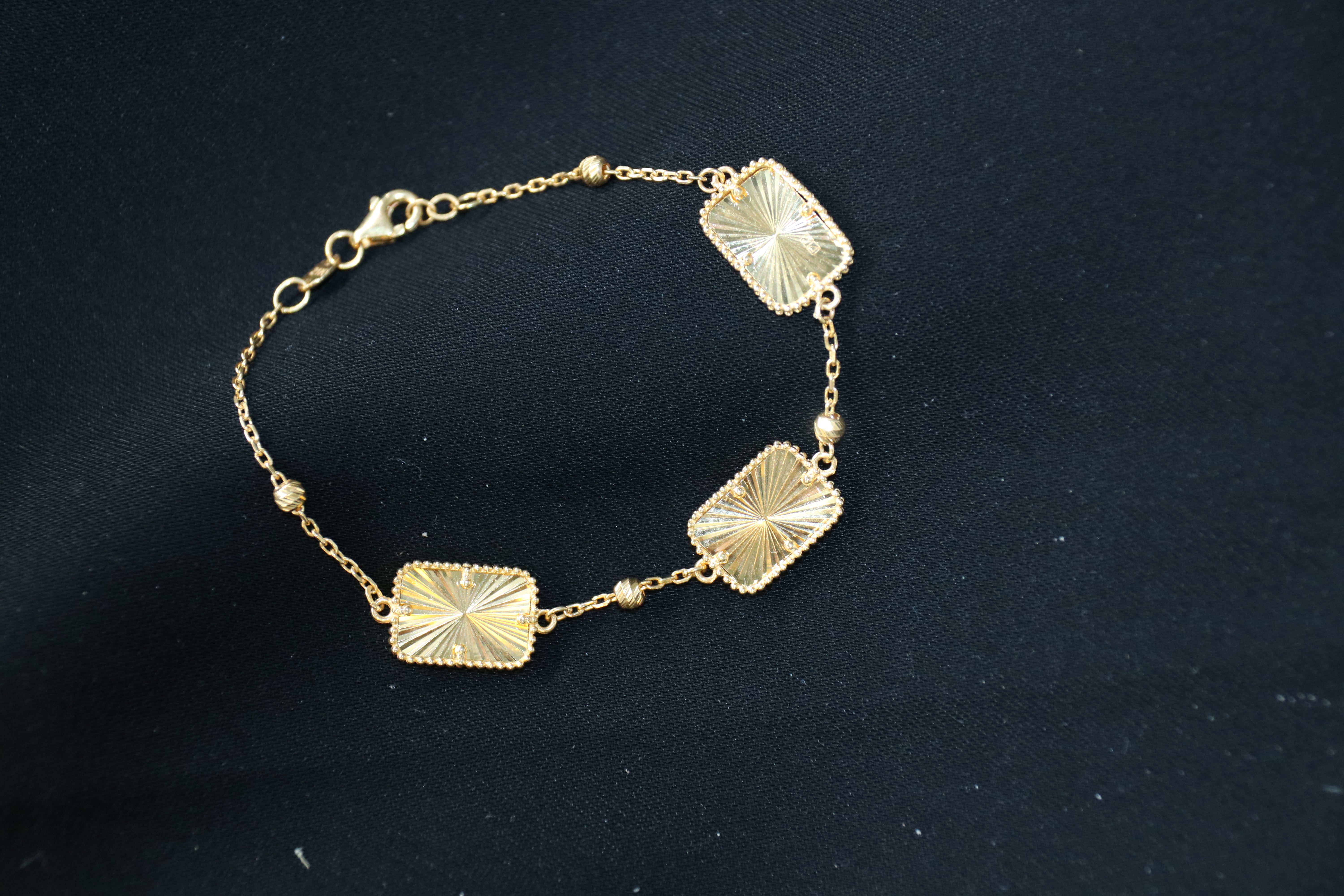 Gold bracelet with square designs on a black background