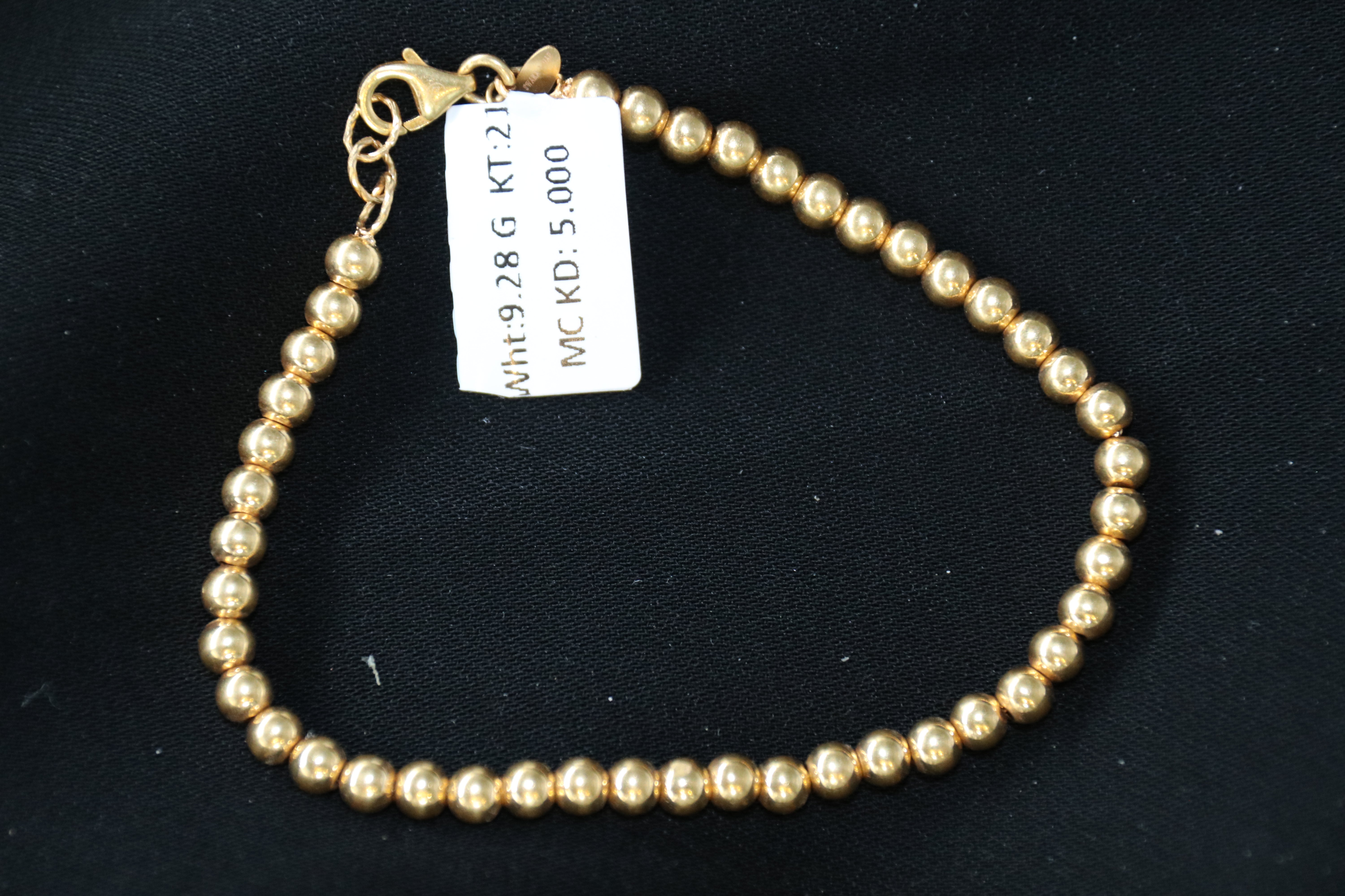 Gold beaded bracelet with a tag on a black background