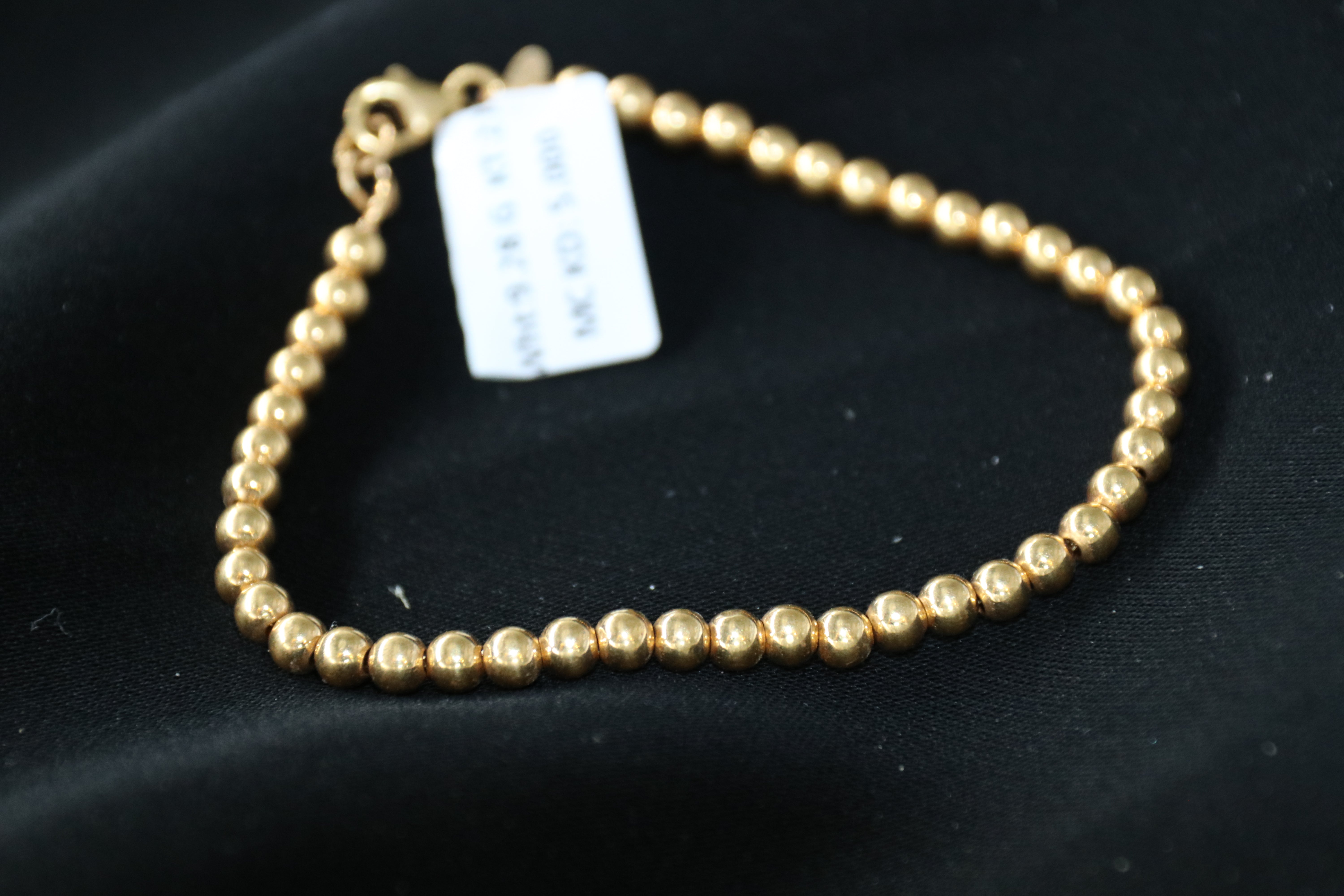 Gold beaded bracelet on a black surface with a label attached.