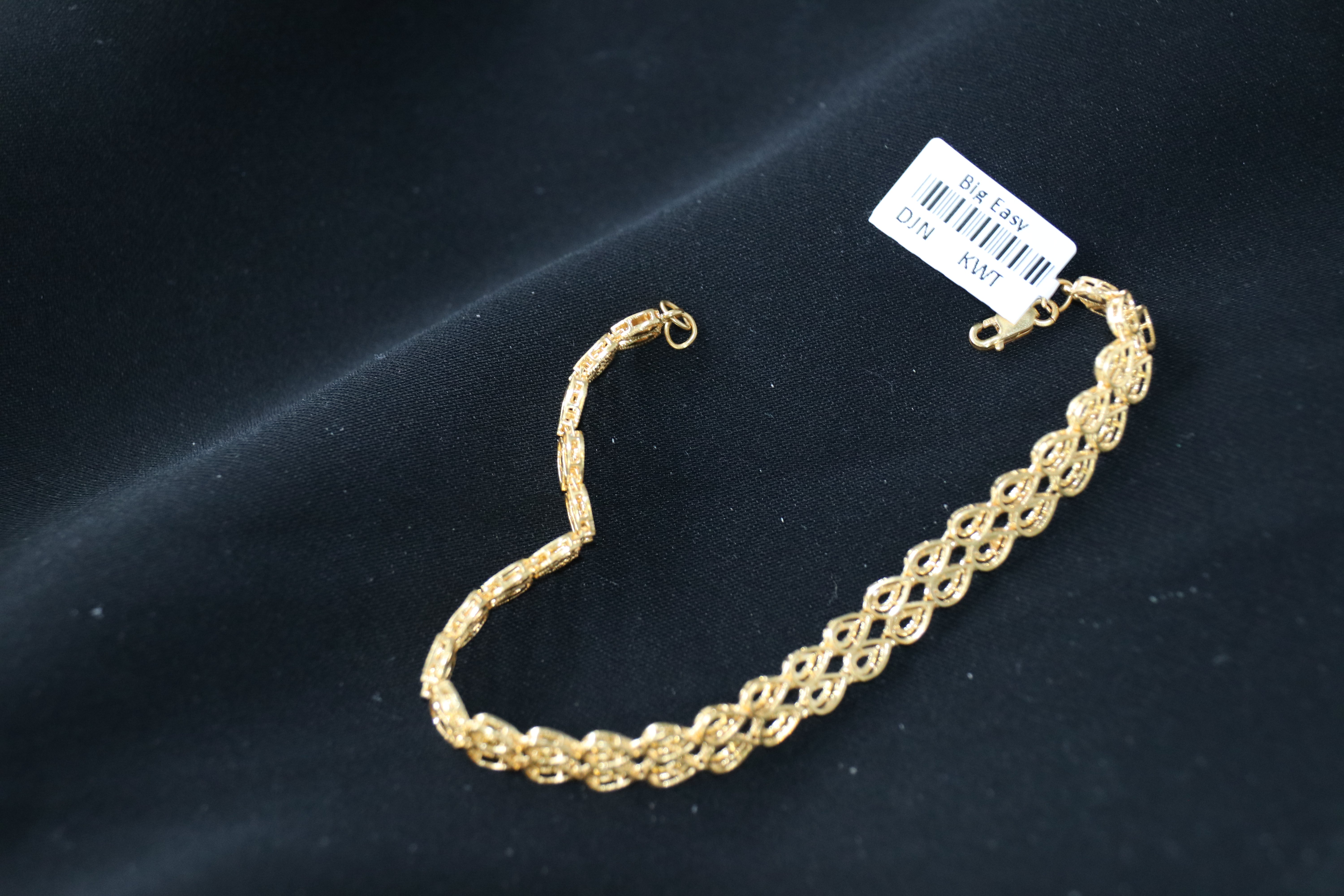 Gold bracelet on a dark background with a visible brand label.