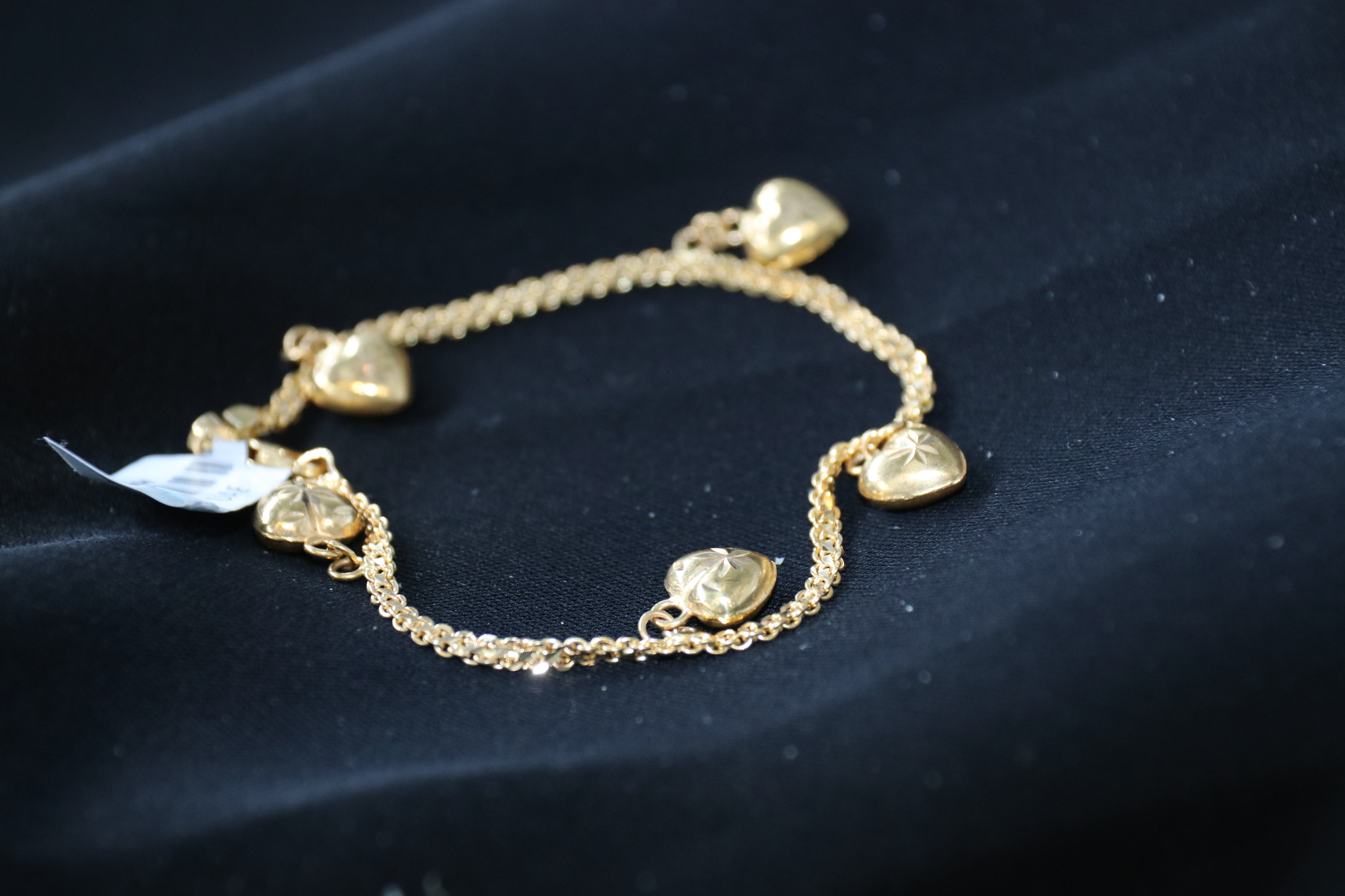 Gold bracelet with heart-shaped charms on a dark background