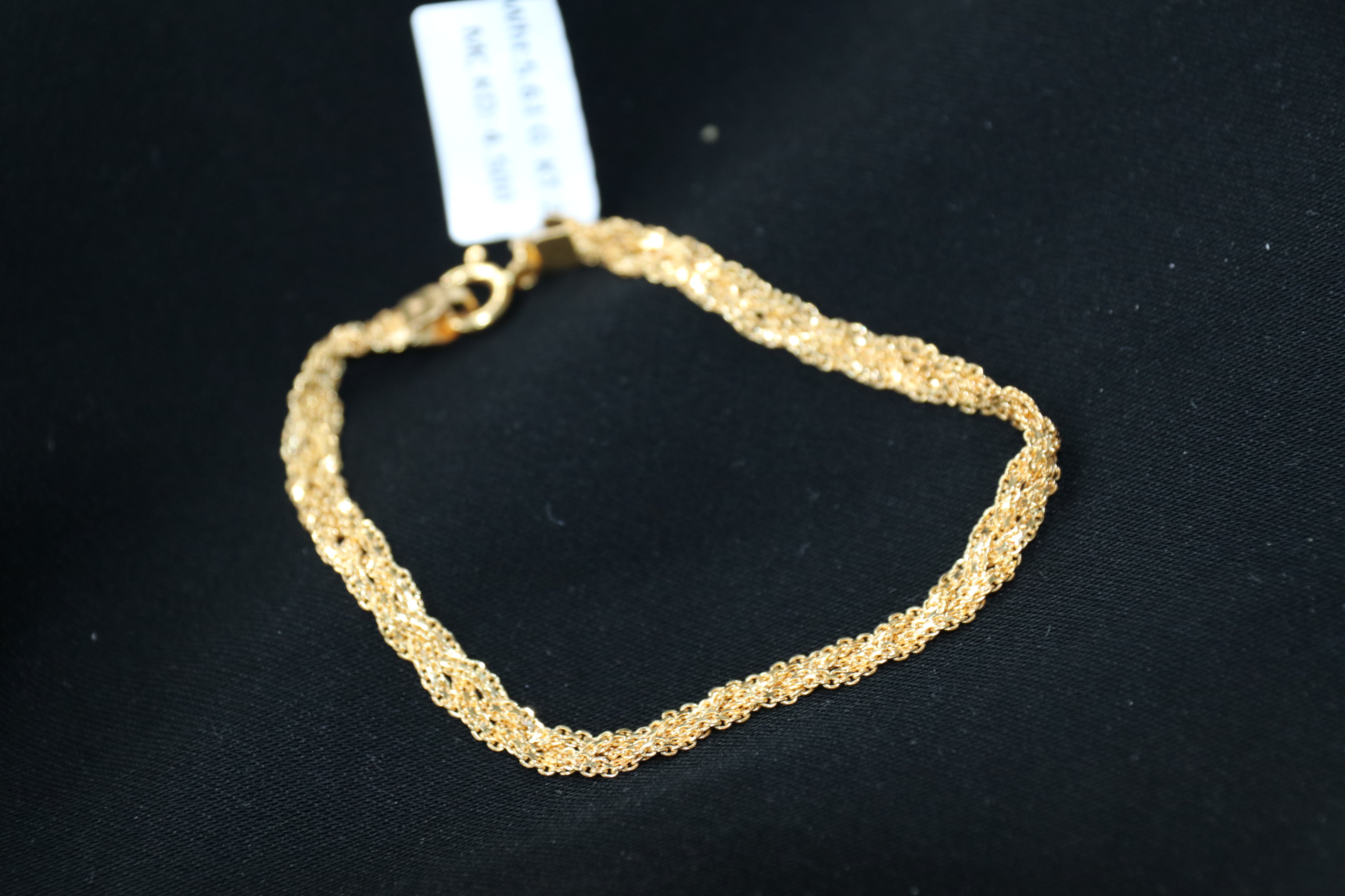 Gold bracelet on a black background with a visible brand tag.