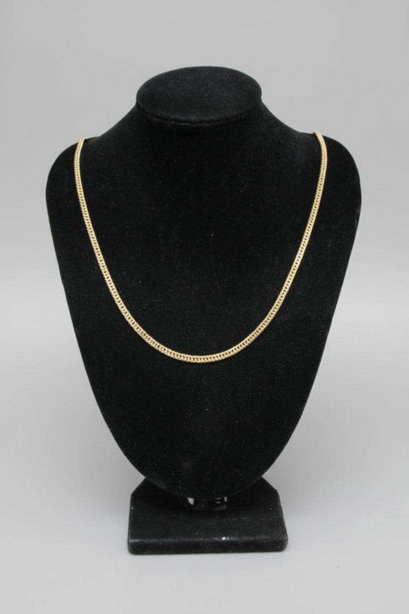 Black hat with gold trim on a mannequin head against a white marble wall.