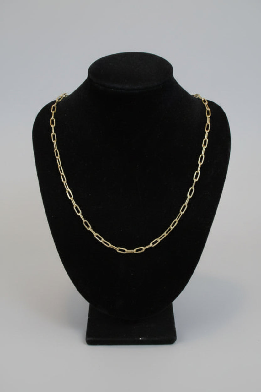 Gold chain necklace on a black velvet stand against a marble wall.
