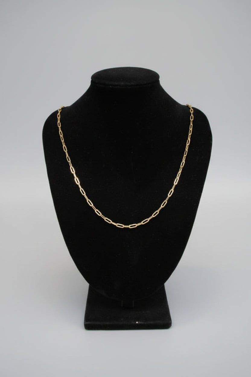 Gold chain necklace on a black velvet stand against a marble wall.