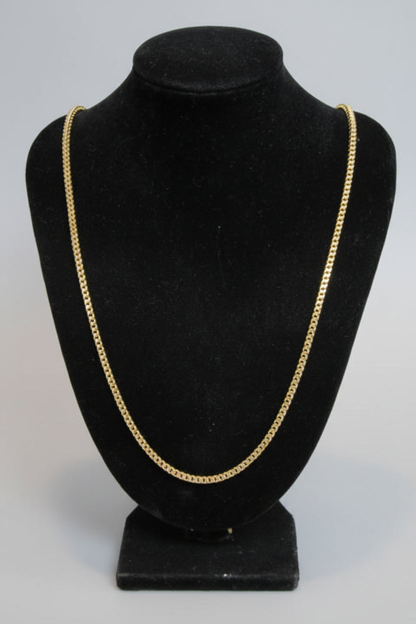 Black hat with gold trim on a mannequin against a marble wall.