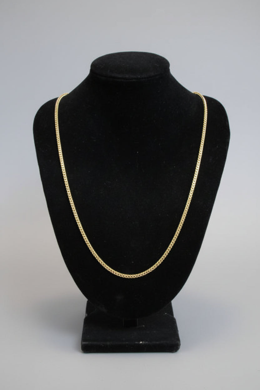 Black hat with gold trim on a stand against a marble wall.