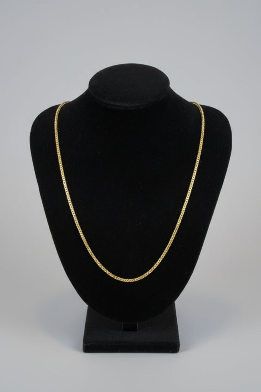 Black hat with gold band on a mannequin against a marble wall.