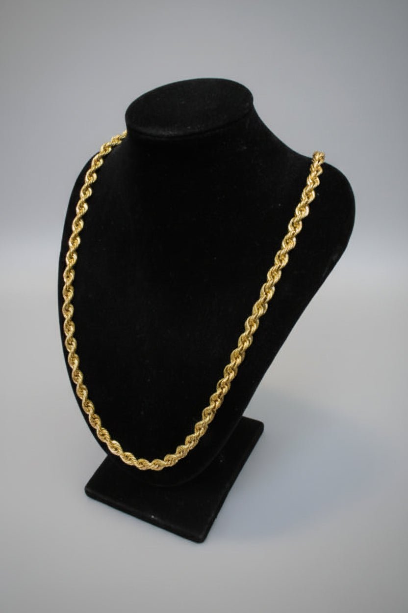 Gold chain on a black cushion against a marble wall