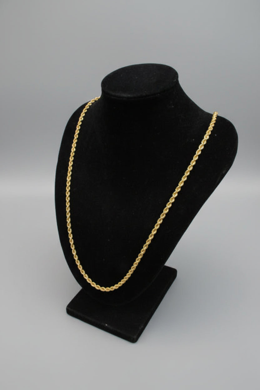 Black hat with gold band on a stand against a marble wall.