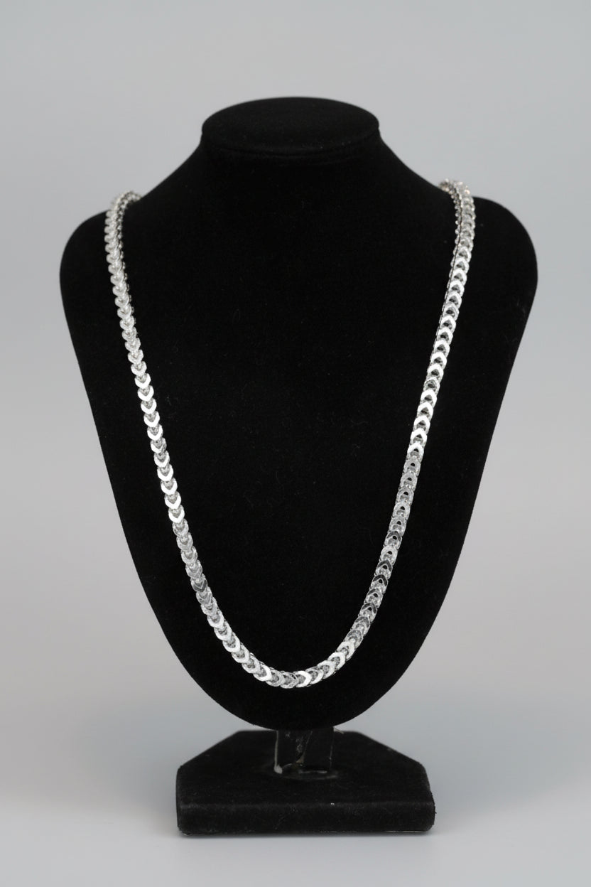 Silver chain necklace on a black bust against a marble surface