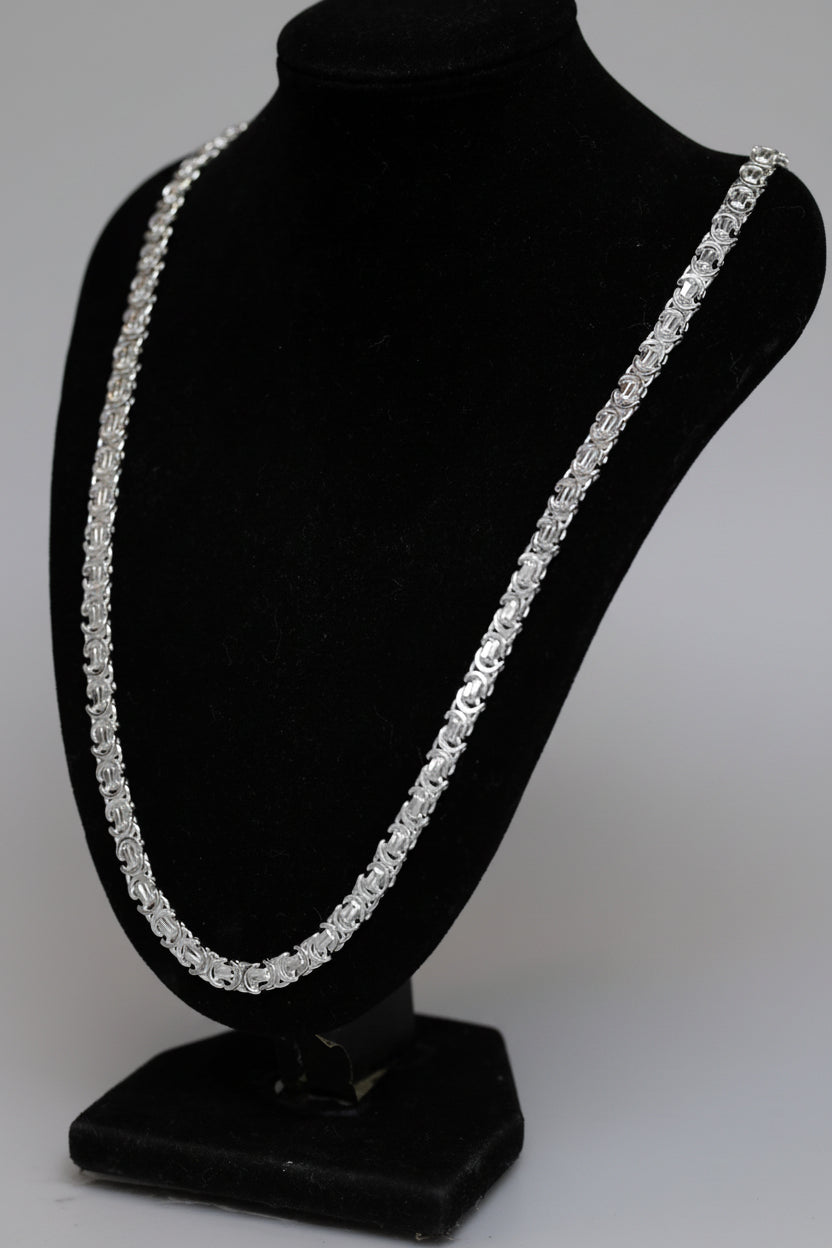 Silver necklace on a black bust against a neutral background