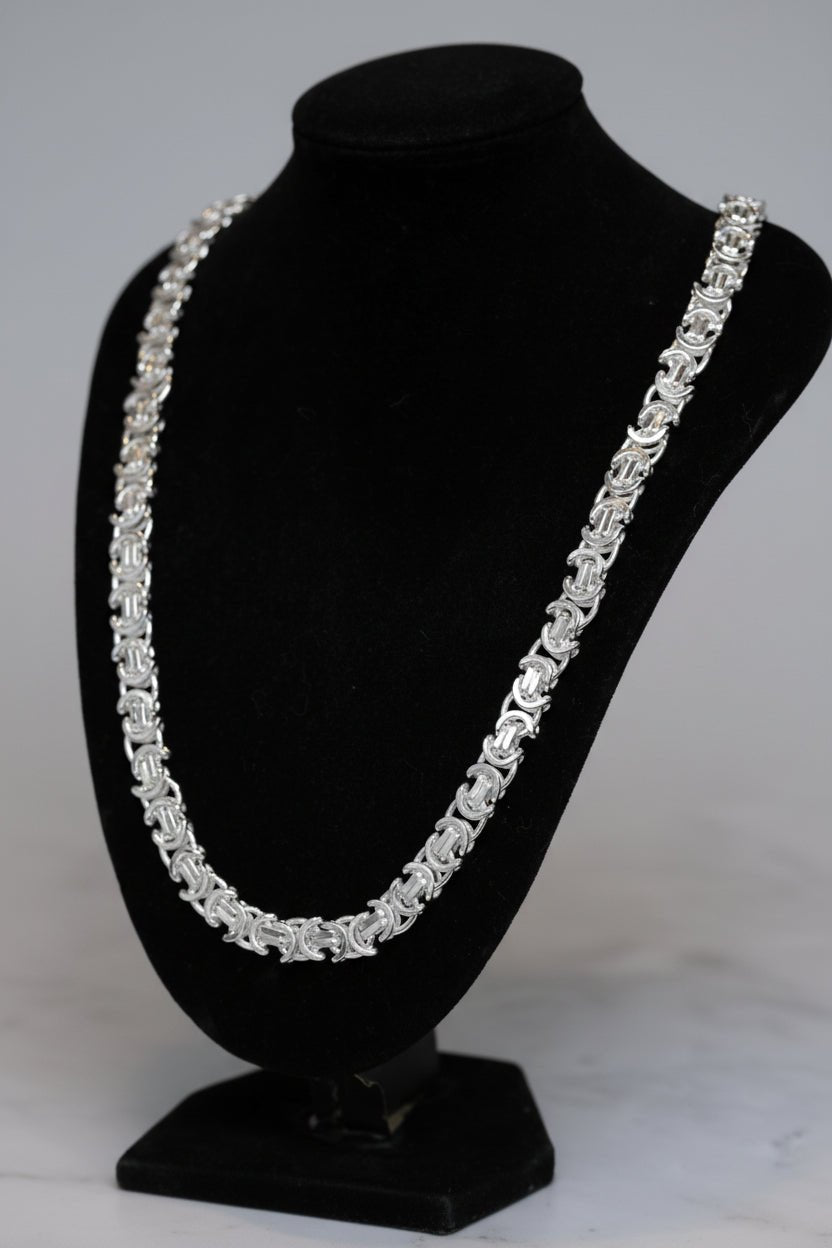 Silver necklace on a black mannequin bust against a dark background