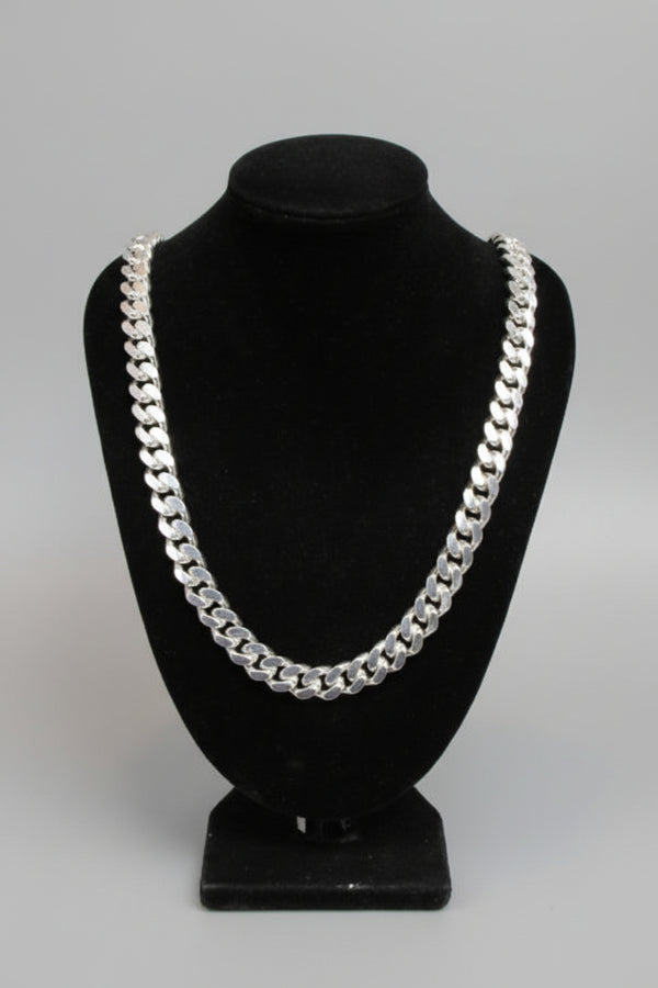 Silver chain necklace on a black velvet stand against a marble wall.