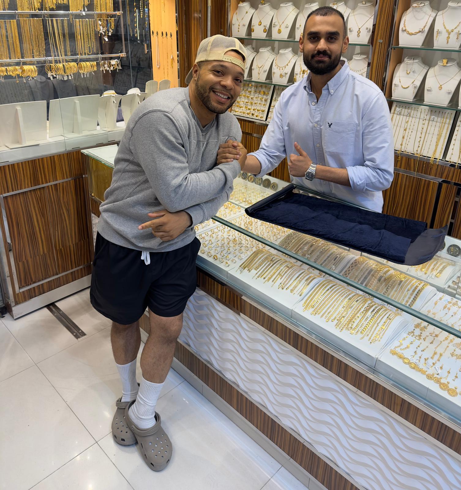 Two men in a jewelry store with gold necklaces on display.