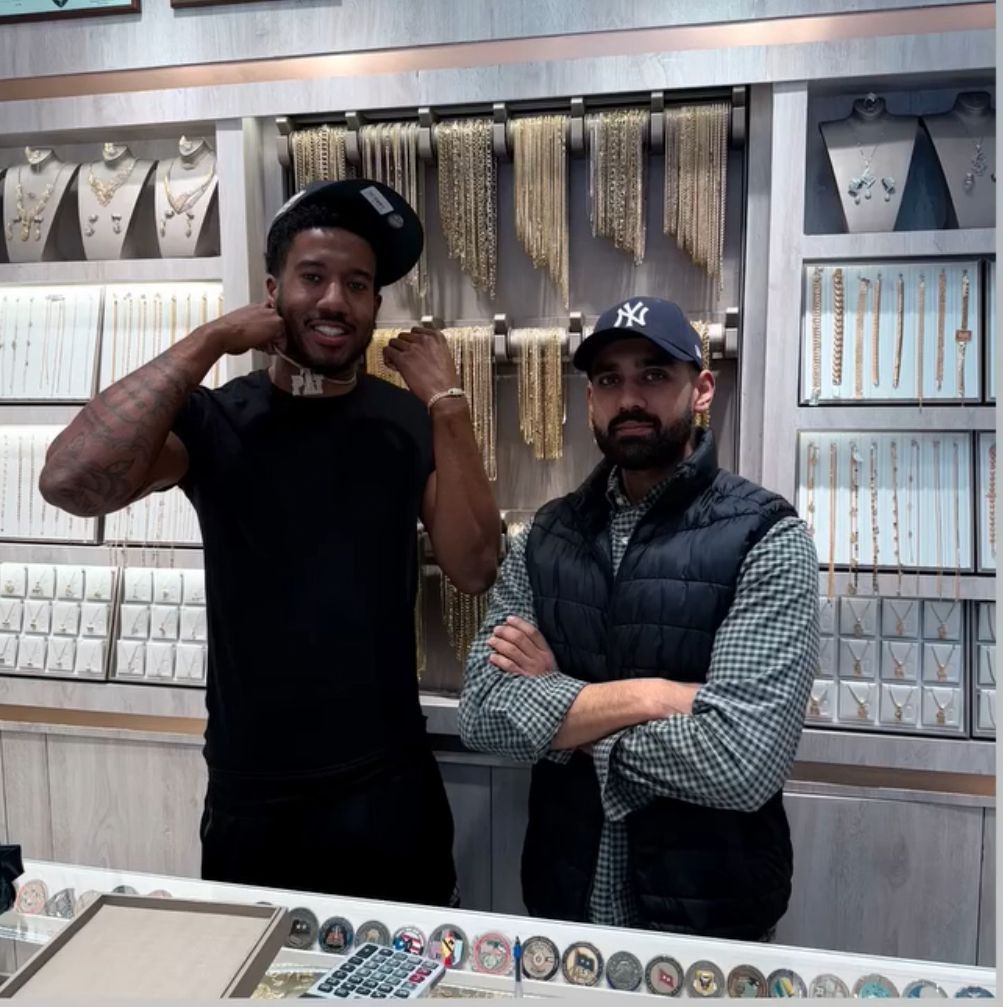 Two men standing in a jewelry store with necklaces on display.